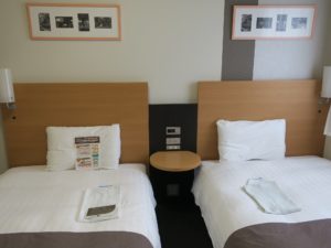 コンフォートホテル秋田 ツインエコノミー ベッド 時計とスイッチ、ACコンセント、サイドテーブルがあります