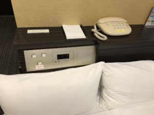 ホテルウィングインターナショナル新宿 シングルルーム 枕元 電話とACコンセント、スイッチ類、時計があります
