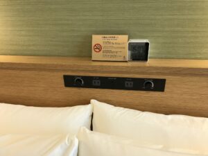 カンデオホテルズ東京新橋 ダブルルーム 枕元 目覚まし時計とACコンセント、照明のスイッチがあります