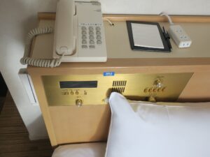 クインテッサホテル伊勢志摩 セミダブルルーム 枕元 時計とラジオ、エアコンと照明のスイッチ、電話機、ACコンセントがあります