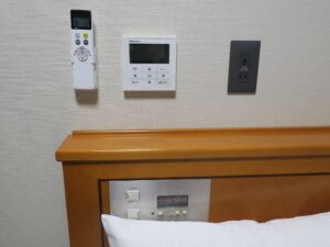 秋田天然温泉 ルートイングランティア秋田 SPA RESORT ダブルルーム 枕元 エアコンと照明のスイッチ、埋め込み式の目覚まし時計、ACコンセントがあります