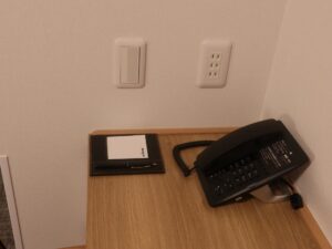ドーミーイン広島ANNEX ダブルルーム デスク横 デスク灯のスイッチとACコンセント、電話、有線LANポートがあります