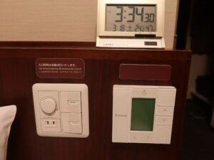 ドーミーイン熊本 セミダブルルーム 枕元 エアコンと照明のスイッチ、ACコンセント、目覚まし時計があります