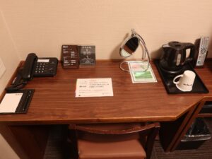 ドーミーイン熊本 セミダブルルーム デスク回り 電話、鏡、電気ポット、マグカップ、液晶テレビとリモコンがあります