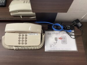 横須賀 セントラルホテル ダブルルーム デスク上 電話機と明かりのスイッチ、ACコンセント、LANケーブル、インターネット/Wi-Fiの接続方法の説明が置いてあります